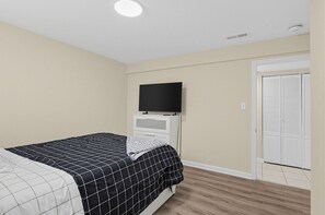 A bedroom with a bed, a television on a dresser, a closet, and a ceiling light.