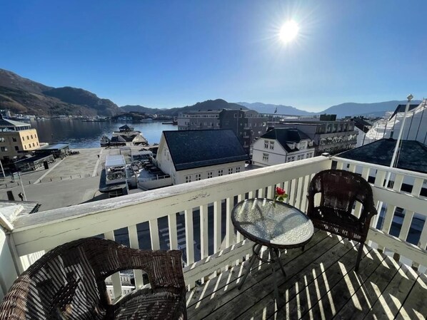 A balcony with wicker furniture, overlooking a harbor with buildings and mountains in the distance. - Jibben Self-Service Hotel (Måløy)