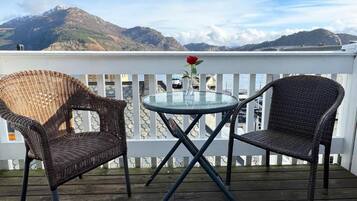 A balcony with wicker chairs and a glass table, overlooking a mountainous landscape.