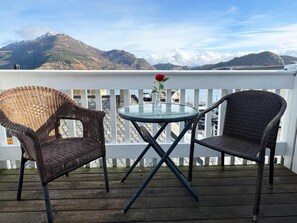 A balcony with wicker chairs and a glass table, overlooking a mountainous landscape. - Jibben Self-Service Hotel (Måløy)