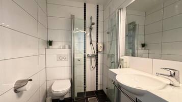 A modern bathroom with a glass-enclosed shower, a white toilet, and a large sink with a mirror.