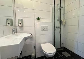 Un baño moderno con lavamanos blanco, inodoro y ducha con cerramiento de vidrio.
