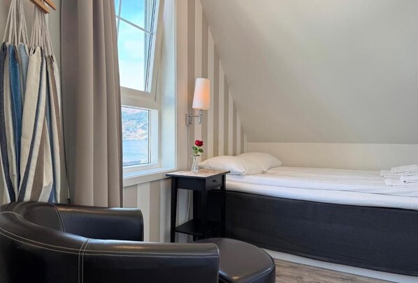 Une chambre d’hôtel avec un lit, une chaise, une table de chevet avec une lampe et une fenêtre avec des rideaux.