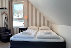A hotel room with a bed, a chair, a lamp, and a window with a view.