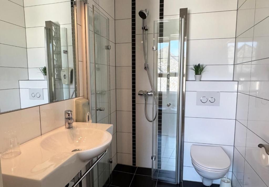 Un baño moderno con ducha envuelta en vidrio, lavamanos blanco y retrete.