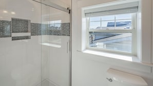 Un baño con cabina de ducha de vidrio, ventana con vista a un edificio y un inodoro con cerradura para mayor privacidad.