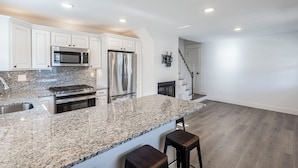 Una cocina moderna con encimeras de granito, electrodomésticos de acero inoxidable y una zona con taburetes de bar.