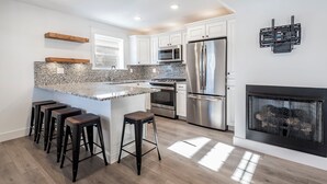 Una cocina moderna con armarios blancos, electrodomésticos de acero inoxidable, encimera de granito y chimenea.