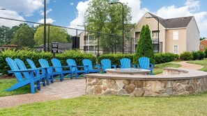 A fire pit area with blue Adirondack chairs and a stone wall. - Williamsburg | Pool & Family Activities | 1BR Suite (Williamsburg)