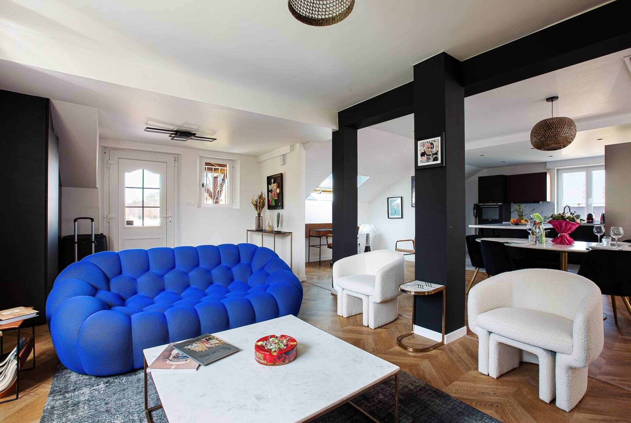 A modern living room with a blue sofa, a white armchair, and a small table with a book and a decorative item.