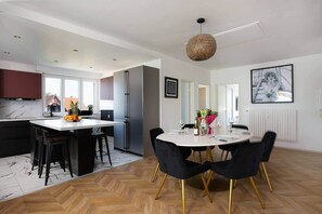 Una cocina moderna con una isla central, un área de comedor con una mesa redonda y sillas, y un ventanal que proporciona luz natural.