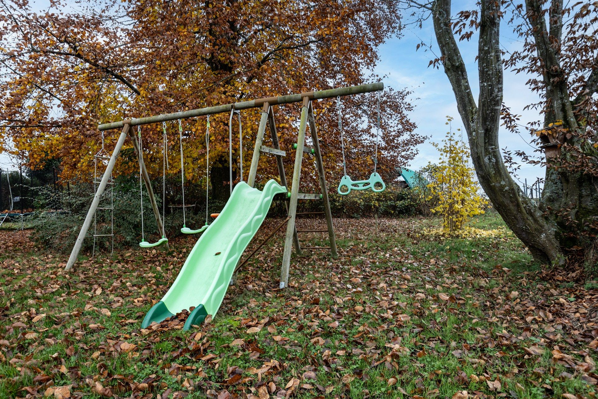 Ein Spielplatz mit Rutsche und Schaukeln, umgeben von Bäumen mit Herbstlaub.