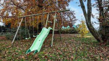 Ein Spielplatz mit Rutsche und Schaukeln, umgeben von Bäumen mit Herbstlaub.
