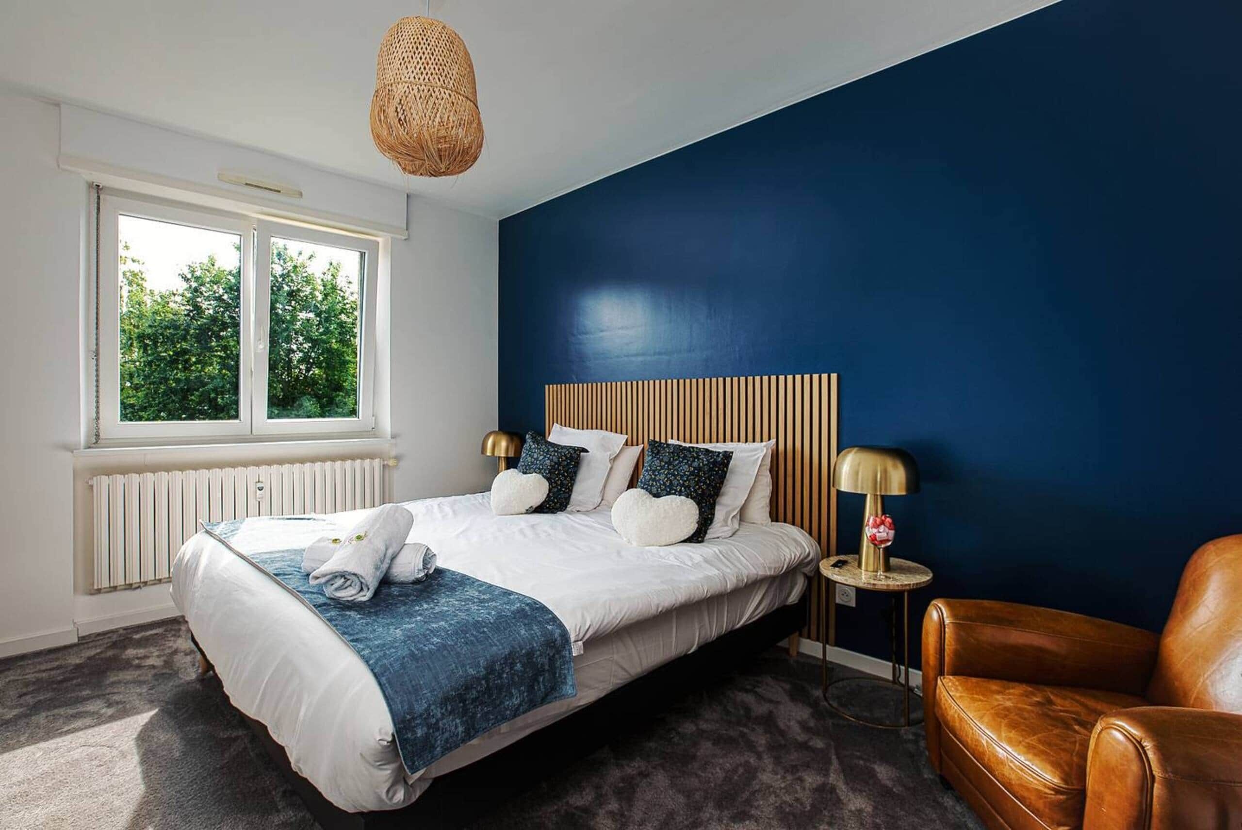 Een slaapkamer met een groot bed, een raam, een stoel en een hanglamp.