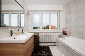 Un bagno moderno con doppio lavabo, vasca e finestra vista edifici.