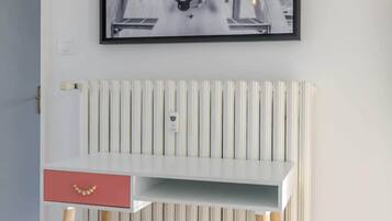 Ein Zimmer mit einem Heizkörper, einem weißen Konsolentisch mit einer roten Schublade und einem gerahmten Bild an der Wand.