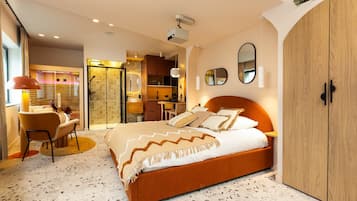 A modern bedroom with a large bed, a wardrobe, a desk, and a shower area.