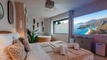 A bedroom with a large bed, a bathtub, and a view of a coastal landscape.