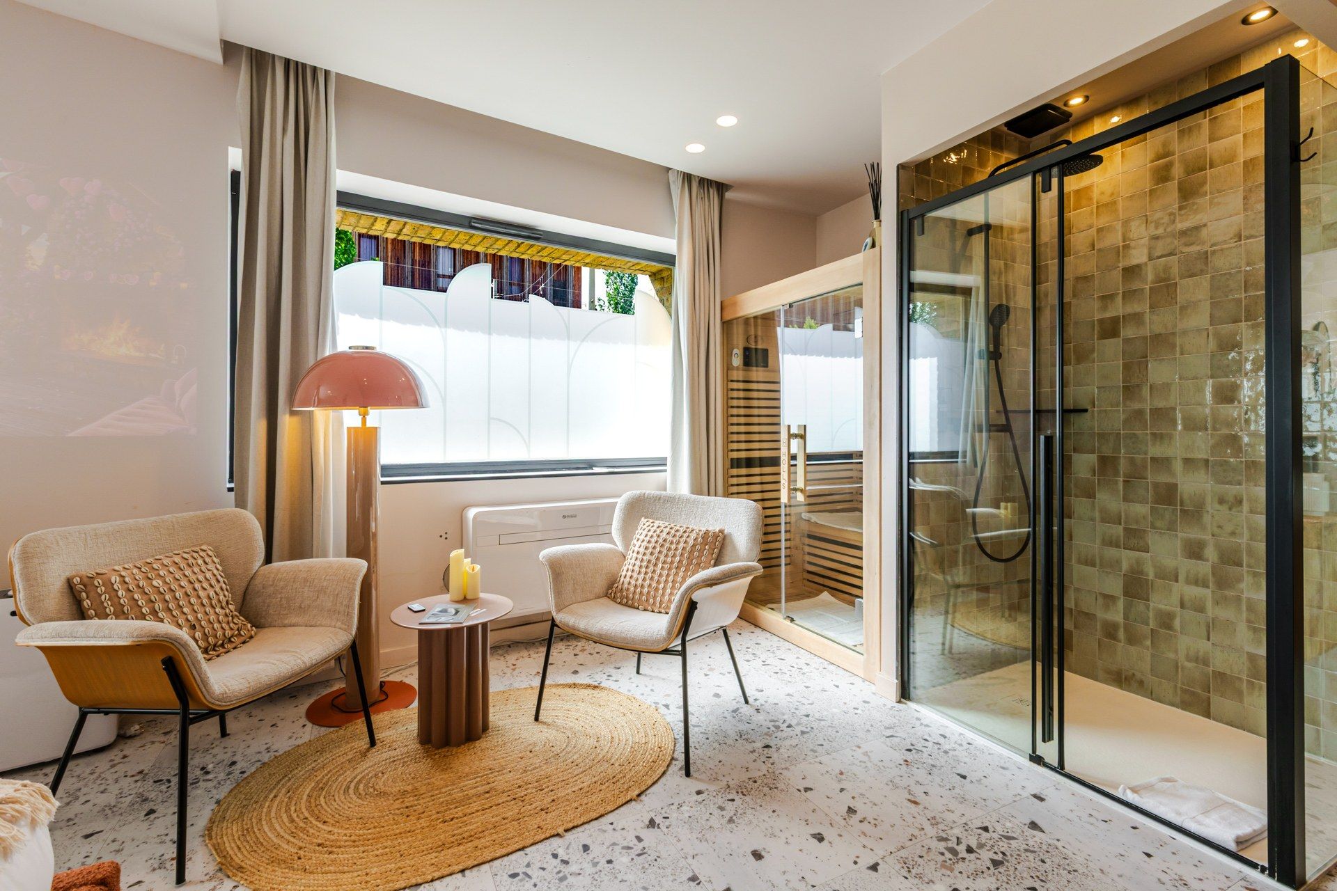 Ein modernes Hotelzimmer mit einer Sitzecke, einer Duschkabine aus Glas und Blick ins Freie.
