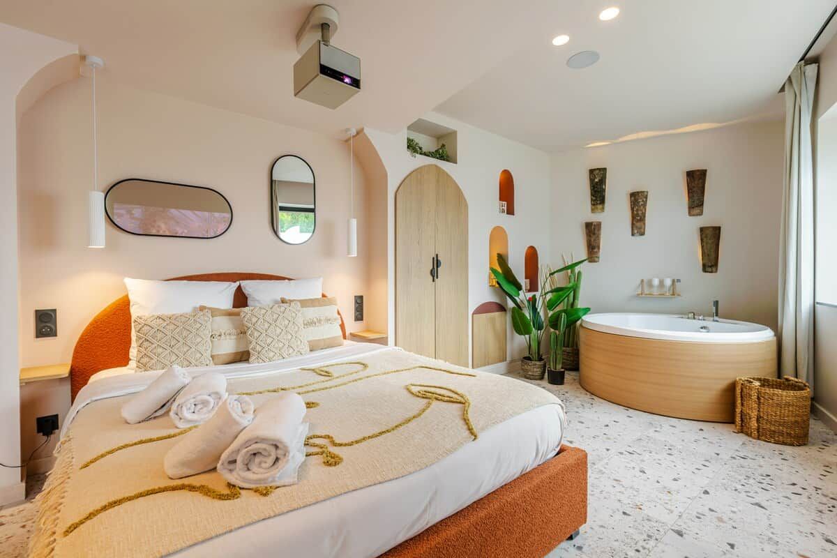 A modern hotel room with a large bed, a round bathtub, and a large mirror.