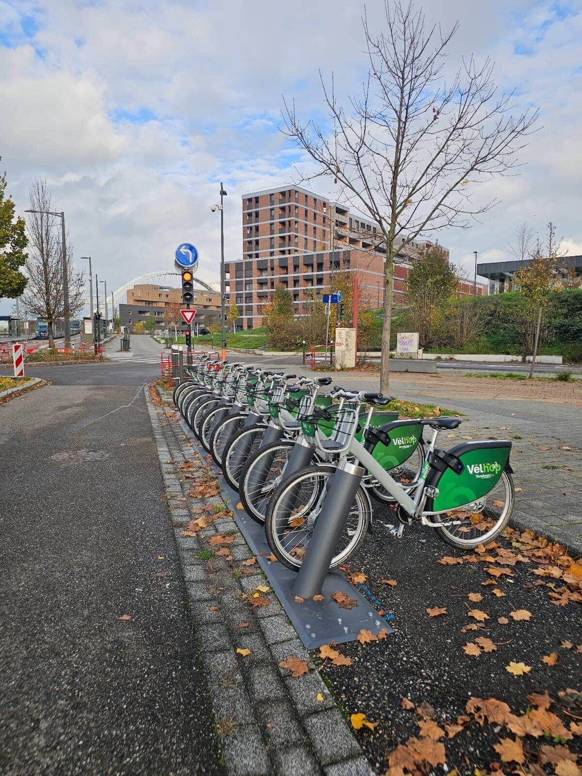 A row of bicycles parked on a bike rack, a traffic light, and a building in the background.