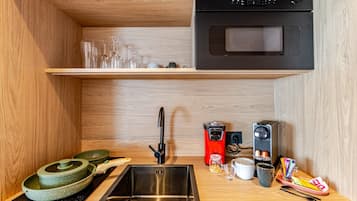 Une petite cuisine équipée comprenant un évier en acier inoxydable, un four à micro-ondes, une machine à café et une petite étagère avec des verres.
