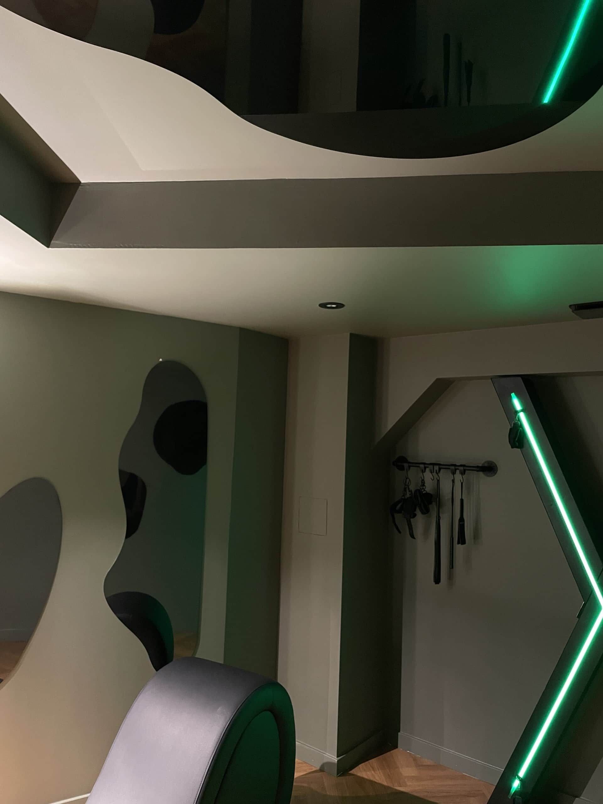 Een modern interieur met een gebogen plafond, een trap met groene verlichting en een muur met abstracte vormen.