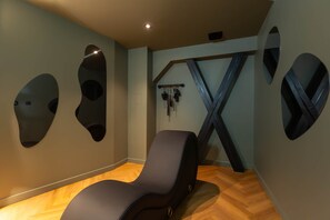 A room with a massage chair, wooden flooring, and wall-mounted exercise equipment. - Romantic Suite in Bali | Jacuzzi | Spa (Strasbourg)