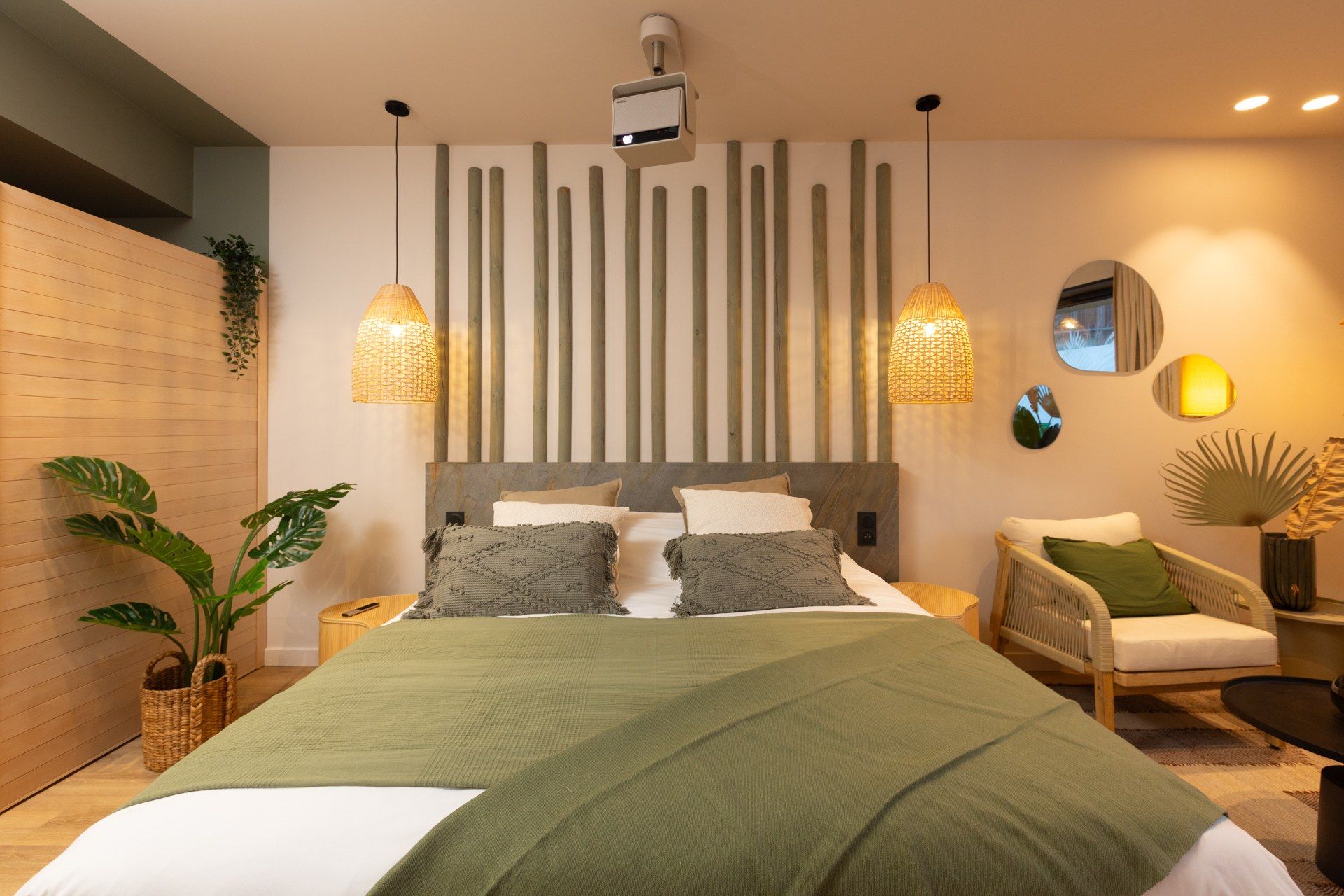 A modern bedroom with a large bed, two bedside lamps, a wall-mounted projector, and a chair with a cushion.