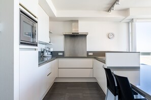 A modern kitchen with white cabinetry, a stainless steel range hood, and a built-in clock. - Apartment by Belgian Coast With Sea Views (Blankenberge)