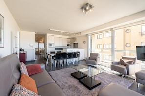 A modern living room with a sofa, coffee table, and chairs, a kitchen in the background, and large windows. - Apartment by Belgian Coast With Sea Views (Blankenberge)