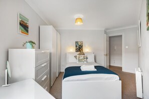 Ein Hotelzimmer mit einem Bett, Nachttischen, einem Kleiderschrank, einem Schreibtisch, einer Lampe und einem Bild an der Wand.