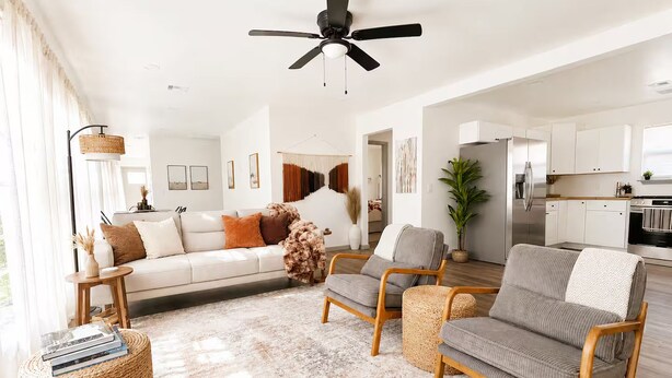 Una sala de estar moderna con un sofá, dos sillones, una mesa de centro y un ventilador de techo.