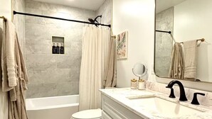 Un baño con bañera, inodoro, tocador con espejo y cortina de ducha.