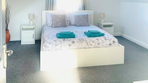 Ein Schlafzimmer mit einem Bett, zwei Nachttischen, einem Fenster mit Vorhängen, einer Hängelampe und einer Topfpflanze.