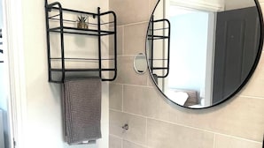 Ein Badezimmer mit einem weißen Waschbecken, einem runden Spiegel, einem Handtuchhalter mit Handtuch und einer Mülleimer.