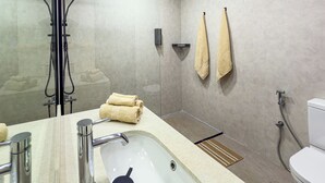 Ein modernes Badezimmer mit einer Glaskabine zur Dusche, einem Waschbecken mit Spiegel und zwei Handtüchern, die an der Wand hängen.