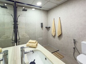 Ein modernes Badezimmer mit einer Glaskabine zur Dusche, einem Waschbecken mit Spiegel und zwei Handtüchern, die an der Wand hängen.