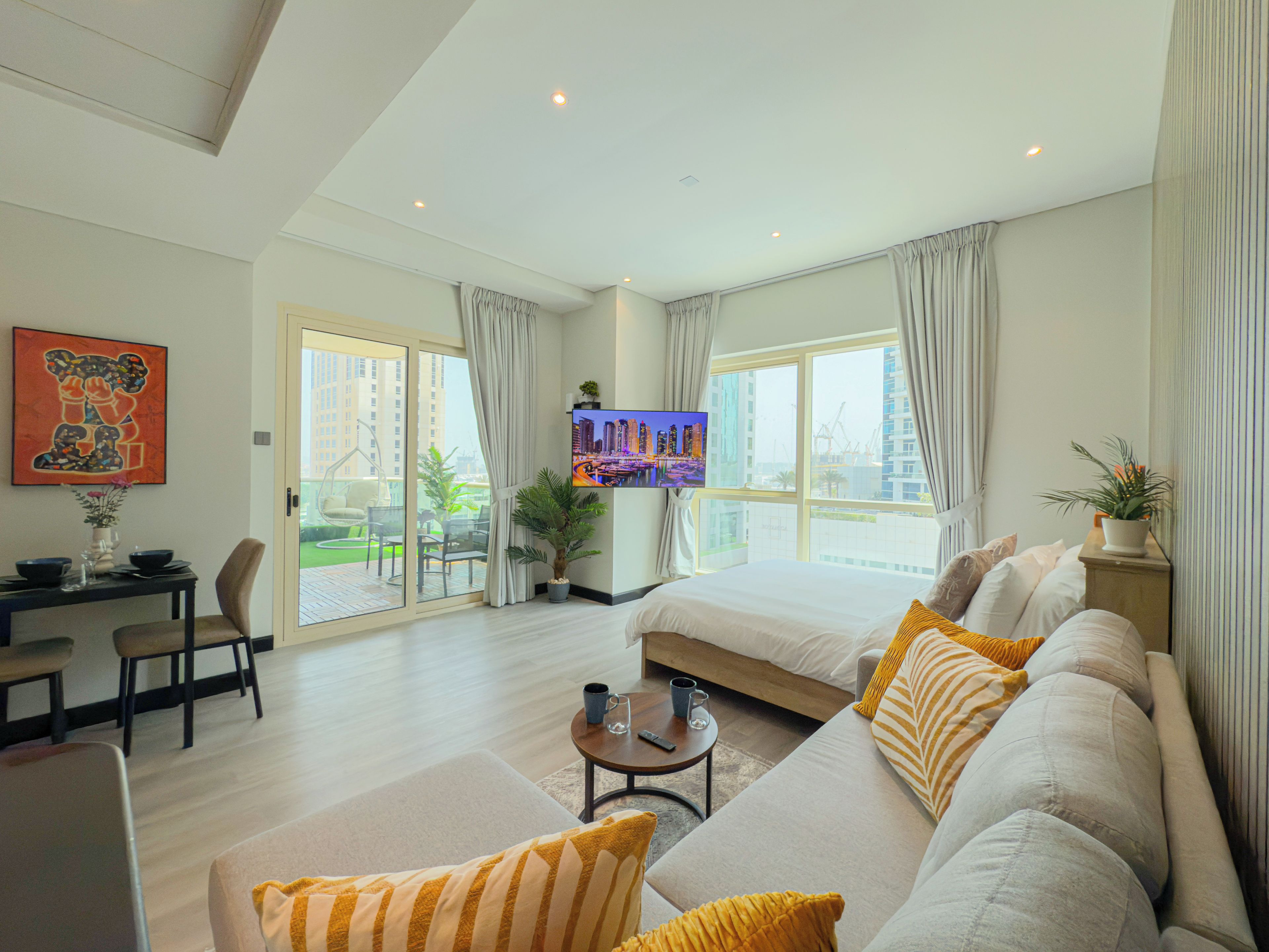 A modern hotel room with a large bed, a sofa, a dining area, and a TV.