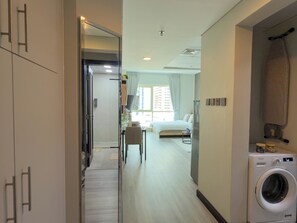 A hotel room with a bed, a desk, a chair, a washing machine, and a large mirror.