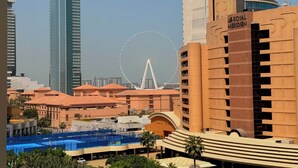 Ein modernes Hotel mit einem markanten Riesenrad im Hintergrund, einem Schwimmbad und einer Mischung aus Hochhäusern und niedrigeren Gebäuden.