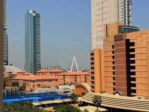Ein modernes Hotel mit einem markanten Riesenrad im Hintergrund, einem Schwimmbad und einer Mischung aus Hochhäusern und niedrigeren Gebäuden.