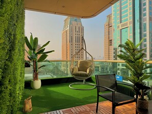 A balcony with artificial grass, a hanging chair, a potted plant, and a view of high-rise buildings.