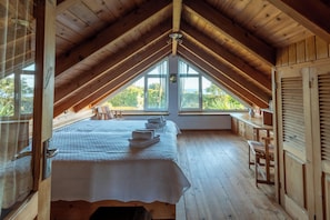 A room with a sloped ceiling, wooden walls, a bed with a white bedspread, a window with a view of greenery, and a wooden table. - Quinta Baviera: Your Charming Retreat with a Jacuzzi on São Miguel Island (Açores)