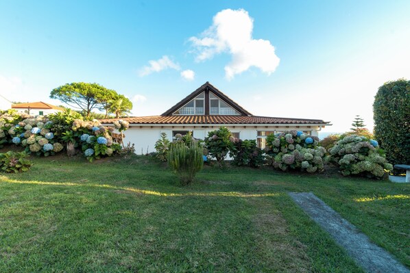 A house with a tiled roof, surrounded by well-maintained hedges and a grassy lawn. - Quinta Baviera: Your Charming Retreat with a Jacuzzi on São Miguel Island (Açores)