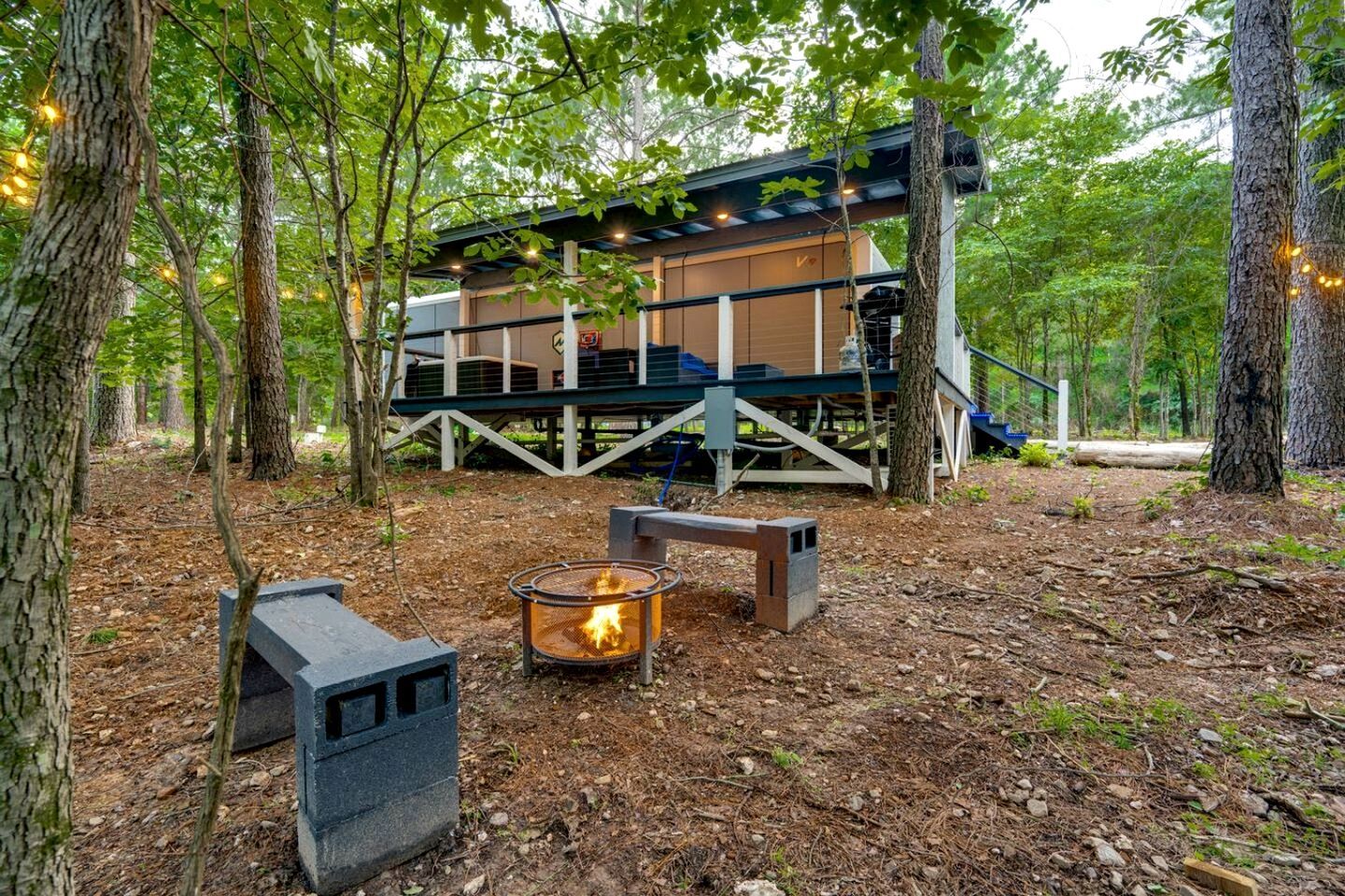A cabin with a deck, a fire pit, and a staircase leading to an upper level.
