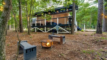 A cabin with a deck, a fire pit, and a staircase leading to an upper level.