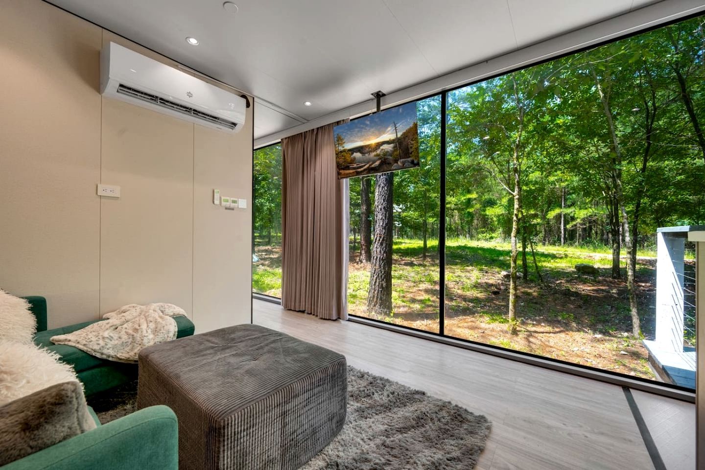 A modern room with a large window, a sofa, a small ottoman, and an air conditioning unit.