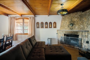 A living room with a stone fireplace, a wooden ceiling, and a large cushioned sofa. - Pousada das Pedras (Camanducaia)