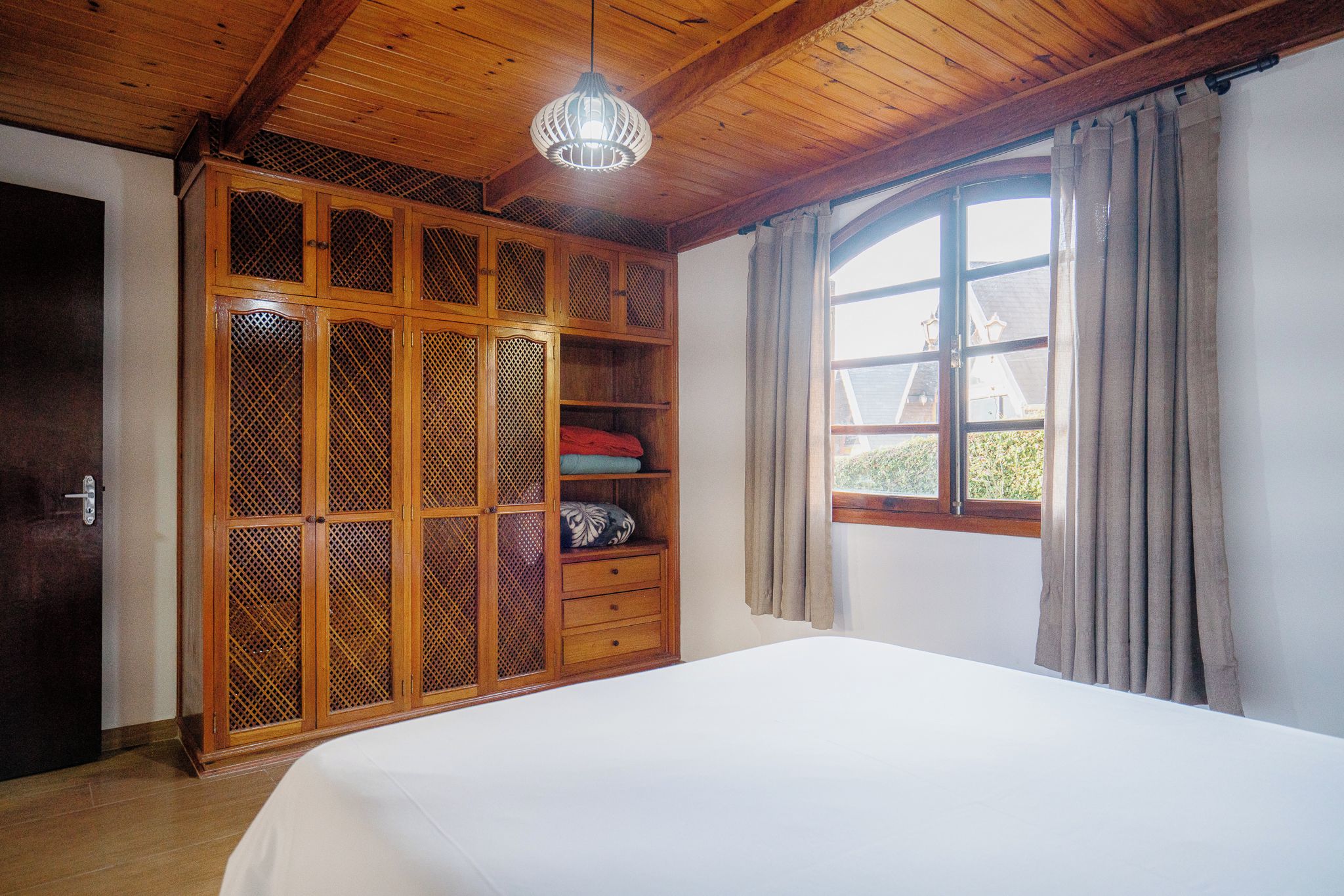 Un dormitorio con un armario de madera, una cama y una ventana con cortinas.